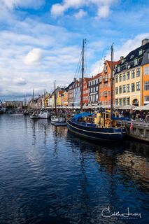 A fine art photograph of the old port of Nyhavn in Copenhagen. Brightly coloured rowhouses and ships with a stunning reflection in the water