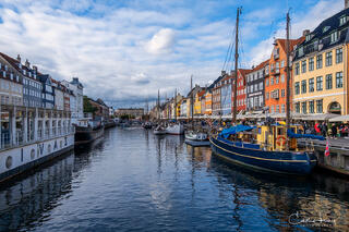A fine art photograph of the old port of Nyhavn in Copenhagen. Brightly coloured rowhouses and ships with a stunning reflection in the water
