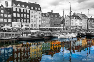 A fine art photograph of the old port of Nyhavn in Copenhagen. Brightly coloured rowhouses and ships with a stunning reflection in the water. 