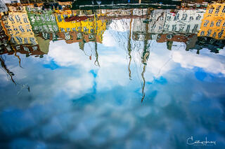 A fine art photograph of the old port of Nyhavn in Copenhagen. Watery reflection ofbrightly coloured rowhouses and ships.