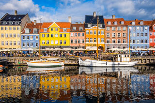 A fine art photograph of the old port of Nyhavn in Copenhagen. Brightly coloured rowhouses and ships with a stunning reflection in the water