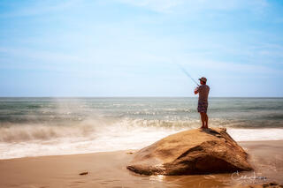A lone fisherman standing on a rock on Aquinnah beach is captured in this long exposure photograph