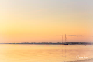golden hour on Fuller street beach in Martha's Vineyard. Oranges reflecting in calm waters with a sailboat in the distance