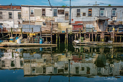 An image of the Portland harbor fish market with reflects of the pier and old colourful, wood buildings along with lobster traps