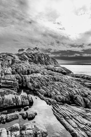 Fine art black and white image of a ragged cliff with houses perched onto overlooking the Norwegian Sea.